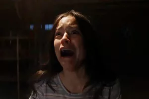 Plan rapproché-épaule sur Jenny Ortega plongée dans le noir, qui hurle, dans le film X.
