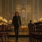 John Wick traverse l'allée entre les chaises en bois d'une grande église, éclairée de très nombreuses bougies ; plan issu du film John Wick : Chapitre 4.