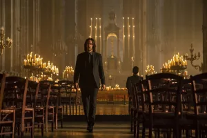 John Wick traverse l'allée entre les chaises en bois d'une grande église, éclairée de très nombreuses bougies ; plan issu du film John Wick : Chapitre 4.