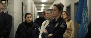 Shailene Woodley en tenue d'officier, attends les bras croisés dans un couloir du commissariat, derrière elle des agents en civil et en uniforme ; scène du film Misanthrope.