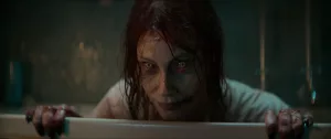 Une femme possédée affiche un sourire malicieux, posant son menton et ses mais sur le rebord d'une baignoire blanche, dans le film Evil Dead Rise.