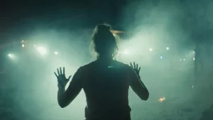 Shailene Woodley vue de dos, en contre-jour, lève les mains en l'air, sous la lumière de lampes torches qu'on devine être celles d'agent de police, dans le film Misanthrope.