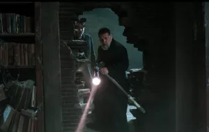 Le père Gabriele Amorth (Russell Crowe) entre dans une pièce via une large fente dans un mur de briques, il doit s'éclairer à la lampe torche dans la pénombre ; scène du film L'exorciste du Vatican.