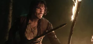 François Civil avance avec méfiance, en sueur, tenant un flambeau dans une main et une épée dans l'autre ; plan issu du film Les Trois Mousquetaires d'Artagnan.
