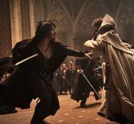 Deux mousquetaires en longue cape à capuche se battent sur le parvis d'une cathédrale dans le film Les trois mousquetaires d'Artagnan.