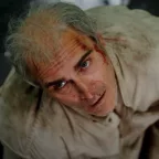 Plongée sur Joaquin Phoenix, du sang sur la tempe, qui regarde au dessus lui l'air perdu, dans le film Beau is afraid.