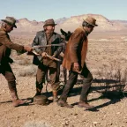 Deux hommes sales en poussent, fusil dans le dos, un troisième dans le désert américain ; scène du film Un nommé Cable Hogue de Sam Peckinpah.