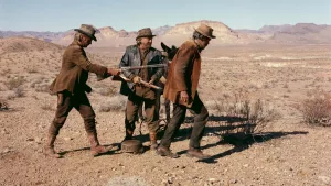Deux hommes sales en poussent, fusil dans le dos, un troisième dans le désert américain ; scène du film Un nommé Cable Hogue de Sam Peckinpah.