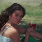 Une adolescente mange une pomme assise dans un parc vert, elle regarde vers nous, dans une moue fermée ; scène du film Sweet sixteen.