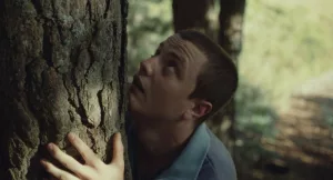 Un jeune homme enlace un arbre, dont il regarde le sommet avec admiration ; plan issu du film Jacky Caillou réalisé par Lucas Delangle.