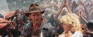 Indiana Jones l'air circonspect, cerné par les autochtones du film Indiana Jones et le temple maudit, qui lèvent les mains vers lui comme une prière.