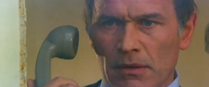 Gros plan sur l'acteur Marcel Bozzuffi, un combiné téléphonique près de l'oreille, l'air perdu dans le film Section de choc.