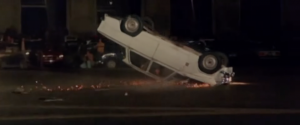 Une voiture blanche se retourne et roule sur le toit, créant des étincelles ; scène de nuit issue du film Section de choc.