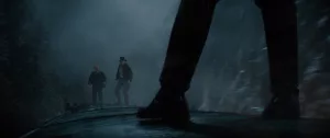 Sur le wagon d'un train qui traverse une zone brumeuse et indéfinissable : au premier plan, deux jambes, à l'arrière plan, au loin, deux silhouettes d'homme dont celle d'Indiana Jones ; scène du film Indiana Jones et le cadran de la destinée.