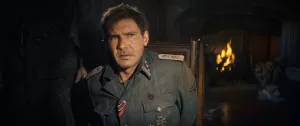 Harrison Ford ligoté à une chaise portant un uniforme Nazi, dans une grotte éclairée par une torche, dans le film Indiana Jones et le cadran de la destinée.