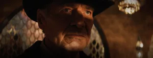 Gros plan sur le visage de Harrison Ford, en contre-jour, portant son chapeau ; une ombre lui coupe le visage en deux ; plan issu du film Indiana Jones et le cadran de la destinée.