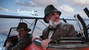 Harrison Ford et Sean Connery dans un avion biplace ; Sean Connery est à l'arrière, et joue les sentinelles pour Indiana Jones qui pilote à l'avant.