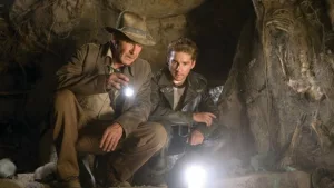 Indiana Jones et son jeune associé joué par Shia LaBoeuf sont dans une grotte, et observent le sol avec des lampes.