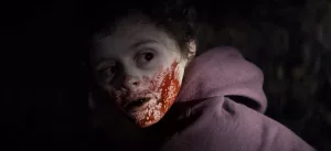 Un enfant pâle, éclairé en contre-jour, a du sang sur toute la joue dans le film Blood.
