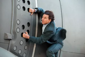 Tom Cruise en costume de ville s'accroche à un avion en plein vol dans le film Mission Impossible : Rogue Nation.