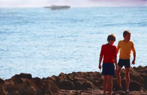 Deux petits garçon, l'un portant un t-shirt jaune et l'autre un t-shirt rouge, au bord de mer, sur les rochers, vus de loin ; plan tourné par Simon Rieth.