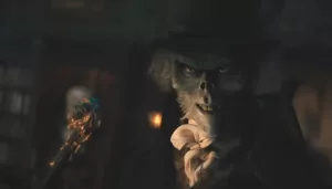 Plan rapproché-épaule sur un fantôme squelette, portant un chapeau haut de forme et tenant dans sa main droite un sceptre avec une tête de mort à son sommet ; issu du film Le manoir hanté.