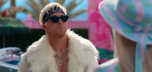 Plan rapproché-épaule sur Ken (Ryan Gosling) l'air arrogant, portant des lunettes de soleil, un bandana noir et une veste en fourrure blanche dans le film Barbie.
