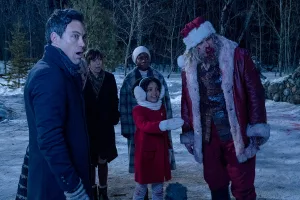 Une petite fille montre du doigt, dans une forêt enneigée, à quatre adultes estomaqués dont un déguisé en Père Noël, quelque chose à l'horizon, dans le film Violent Night.