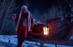 Un Père Noël tout tâché de sang pose fièrement près de son traineau, une hache sur l'épaule ; plan issu du film Violent Night.