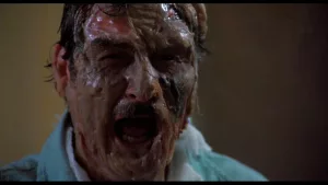 Plan rapproché-épaule sur nu visage d'homme attaqué par l’acide, l'homme hurle tandis que sa peau se met à culer ; issu du film Le monstre qui vient de l'espace.