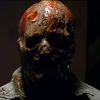 Plan rapproché-épaule en contre-jour sur un homme dont la peau a fondu, ne reste que son crâne et un peu de sang et de chair marron, coulante ; issu du film Le monstre venu de l'espace.