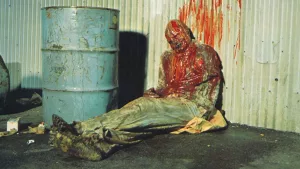 Un cadavre ensanglanté et décharné gît assis contre la façade d'un entrepôt dans le film Le monstre qui vient de l'espace.