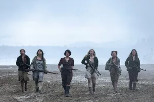 Six femmes armées, se dirigent vers nous alignées, prêtes au combat ; elles avancent dans une plaine grise et brumeuse, l'horizon derrière elle, fait de ce qui semble être une forêt, est à peine perceptible ; scène du film Sisu : de l'or et du sang.