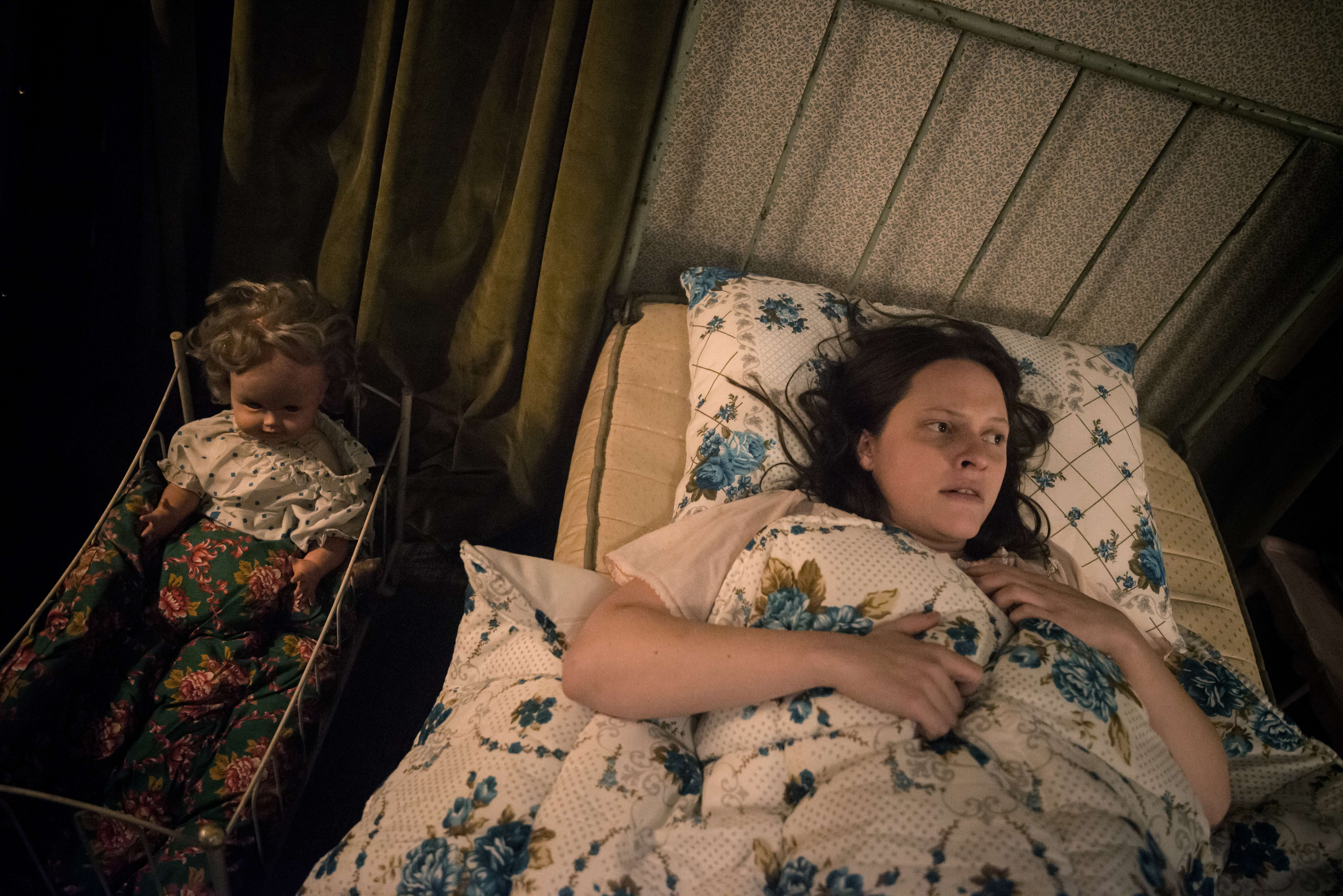 Une jeune femme est allongée dans son lit ancien, l'air anxieux ; à ses côtés, une poupée, ancienne elle aussi, dans un vieux berceau ; scène du film Megalomaniac.