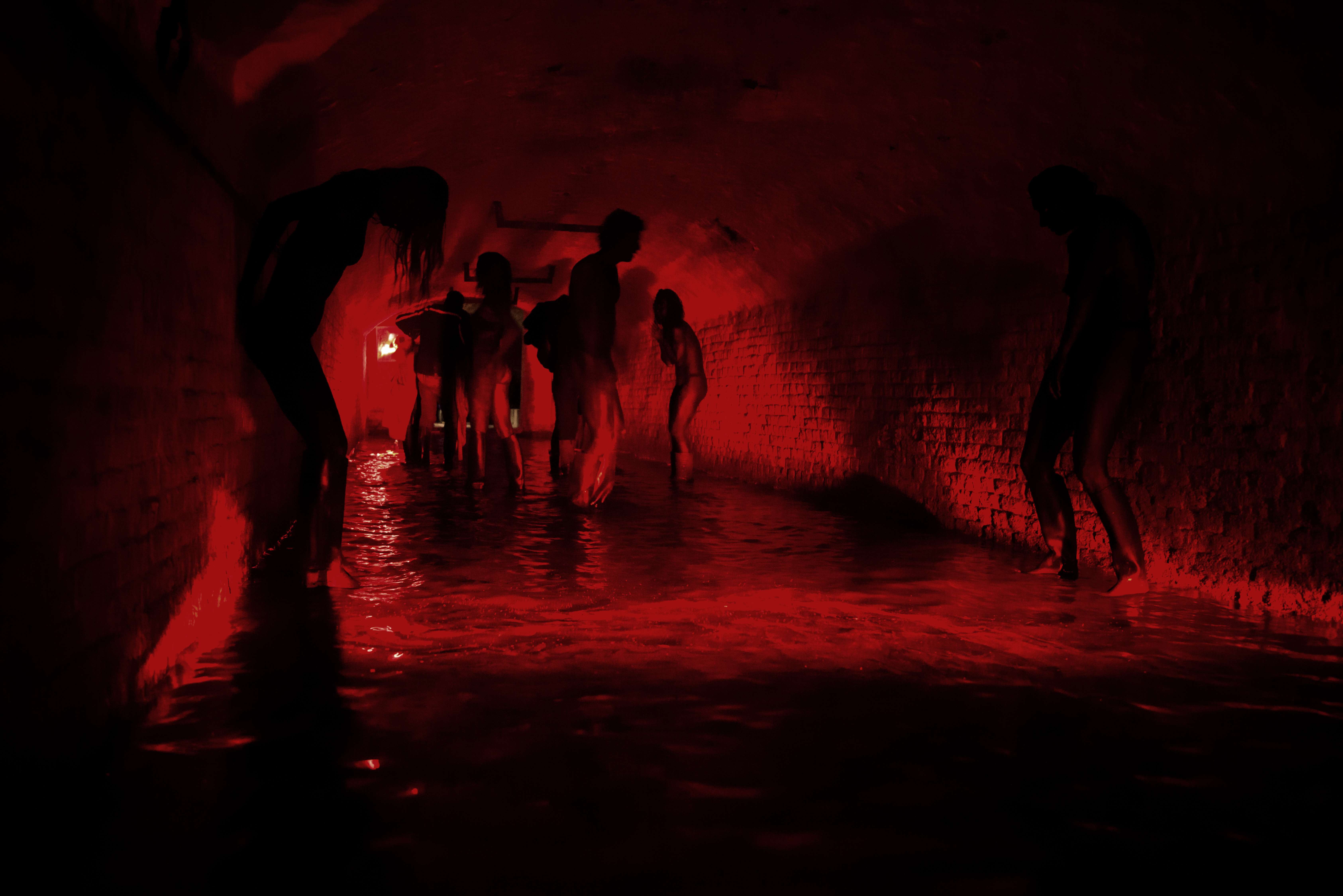 Des silhouettes errent tête baissée dans un tunnel d'égout plongé dans une lumière rouge dans le film Megalomaniac.