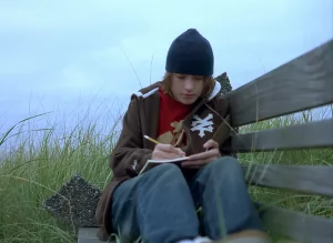 Gabriel Nevins écrit sur un banc au milieu de l'herbe, bonnet sur la tête, sous un ciel gris, dans le film Paranoid Park.