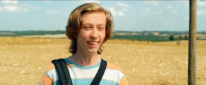 Plan rapproché-épaule sur Pierre Gommé souriant et benêt sur un fond de champ jauni par le soleil dans le film Super-bourrés.