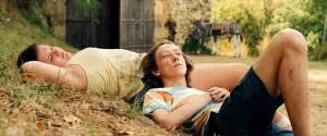 Janus et Sam sont allongés sur l'herbe, le premier la tête posée sur la cuisse de la seconde ; tous deux regardent le ciel, pensifs ; plan tourné par Bastien Milheau.