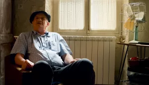 Jean Lassalle assis, béret noir sur la tête, dans un tout petit salon ensoleillé, face au radiateur et à un vieux ventilateur, filmé par Bastien Milheau.