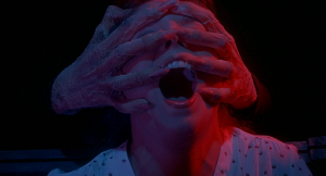 Deux mains monstrueuses saisissent un visage d'homme qui crie, dans le film Inferno de Dario Argento.