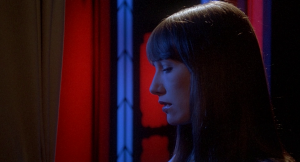 Plan rapproché-épaule sur Daria Nicolodi, vue de profil, la tète baissée,; songeuse, plongée dans une lumière bleue et rouge peu réaliste ; issu du film Inferno.