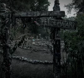 Un vieux panneau en bois indique Pet Cemetary, devant le sinistre et gris cimetière pour animaux du film Simetierre : aux origines du mal.