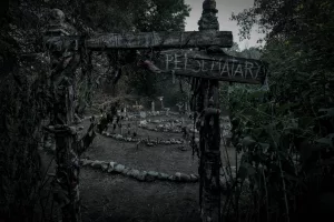 Un vieux panneau en bois indique Pet Cemetary, devant le sinistre et gris cimetière pour animaux du film Simetierre : aux origines du mal.