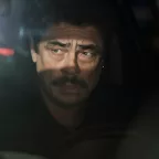 Benicio Del Toro soucieux au volant d'un véhicule, plongé dans l'ombre ; seul ses yeux sont éclairés par le soleil qui luit derrière lui ; plan issu du film Reptile.