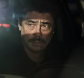 Benicio Del Toro soucieux au volant d'un véhicule, plongé dans l'ombre ; seul ses yeux sont éclairés par le soleil qui luit derrière lui ; plan issu du film Reptile.
