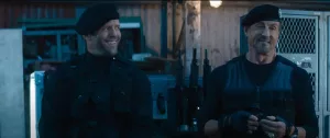 Jason Statham et Sylvester Stallone côte à côte, souriants, mais en sobre tenue de combat noire, devant une supérette, dans le film Expendables 4.