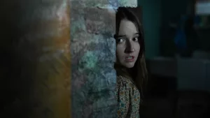 Une jeune femme apeurée se cache derrière un mur ; scène de nuit du film Traquée.