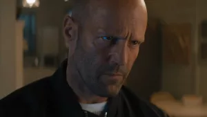 Plan rapproché-épaule sur un Jason Statham renfrogné et soucieux, dans son salon, issu du film Expendables 4.