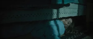 La jeune Mandy se cache sous son lit, en pleine nuit, dans le film Traquée.