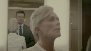Un échange entre une vielle femme et Justin Timberlake ; nous voyons au premier plan le regard suppliant de la vielle femme, floue ; au second plan le reflet de Timberlake, droit, en costume, dans un miroir ; plan extrait du film Reptile disponible sur Netflix.